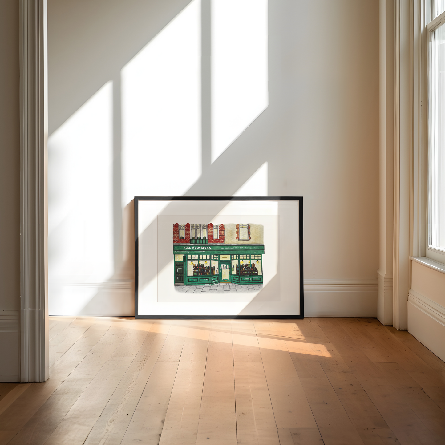 Framed artwork of a building on a wall in a bright room with sunlight streaming through windows.