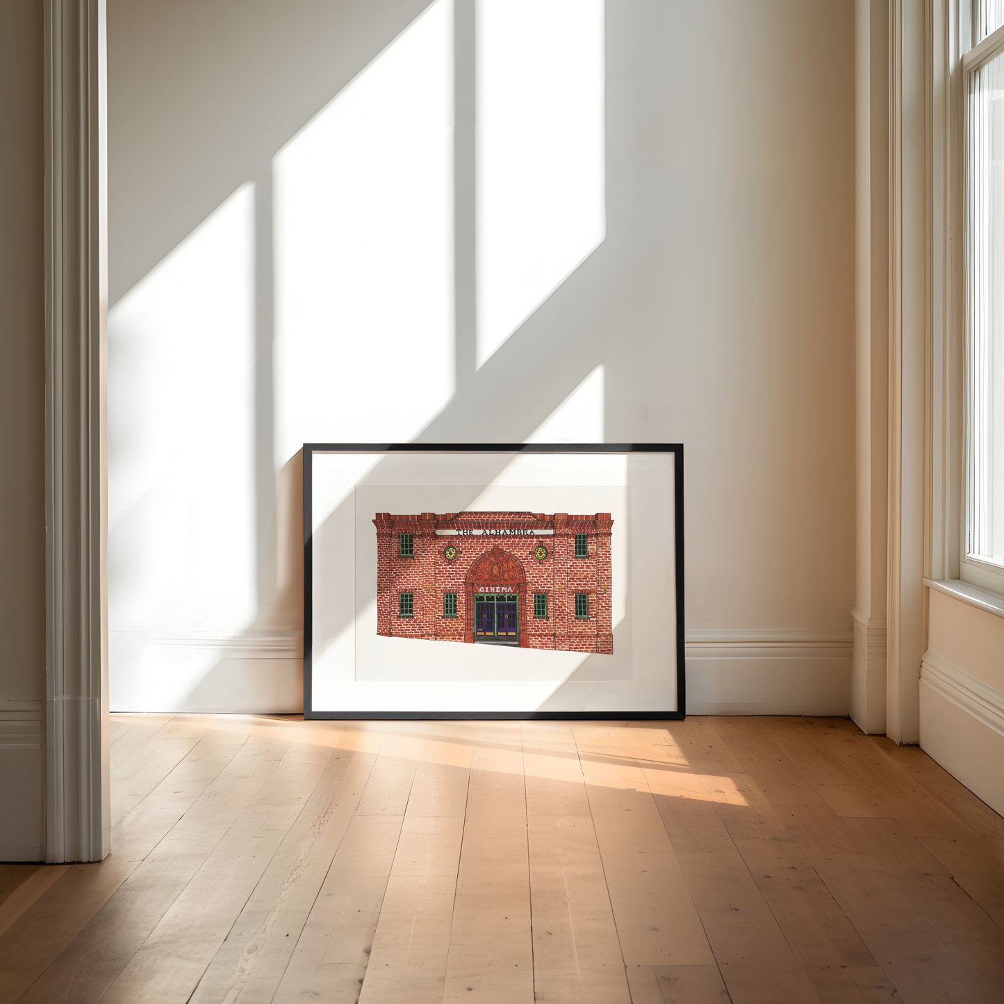 Framed print of a red brick building in a bright room with large windows.