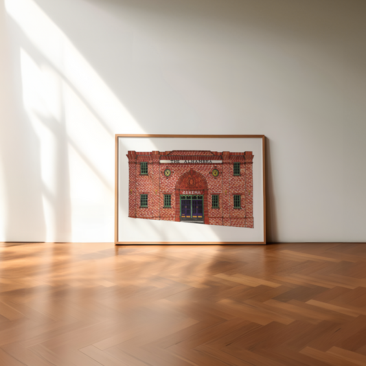Framed artwork of a brick building on a white wall with wooden floor