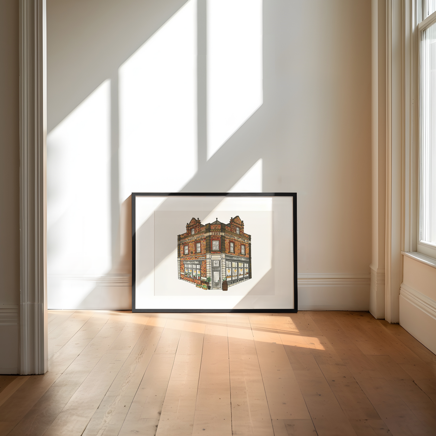 Framed artwork of a building on a wall in a bright room with sunlight streaming through windows.