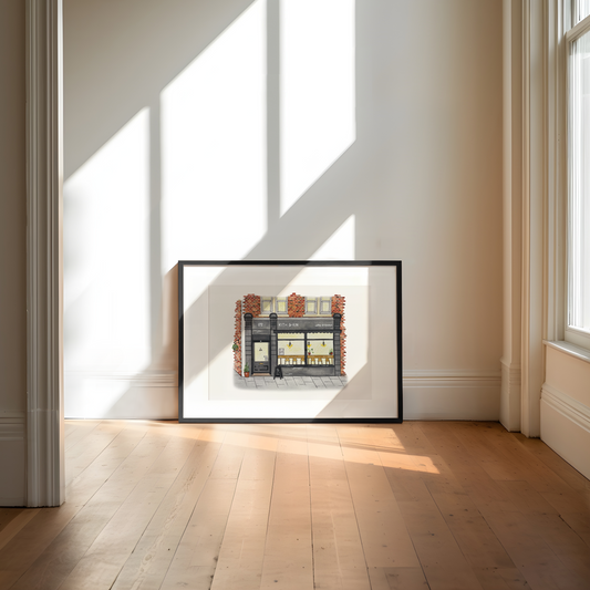 Framed artwork of Kith and Kin cafe on a wall in a bright room with sunlight streaming through windows.