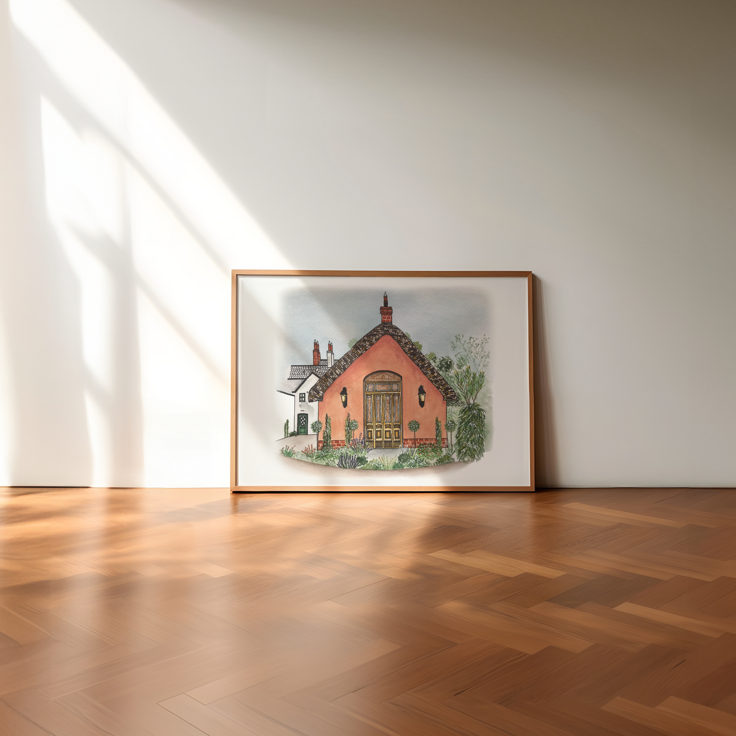 Framed artwork of le Petit Château wedding venue on a wooden floor with sunlight casting shadows.
