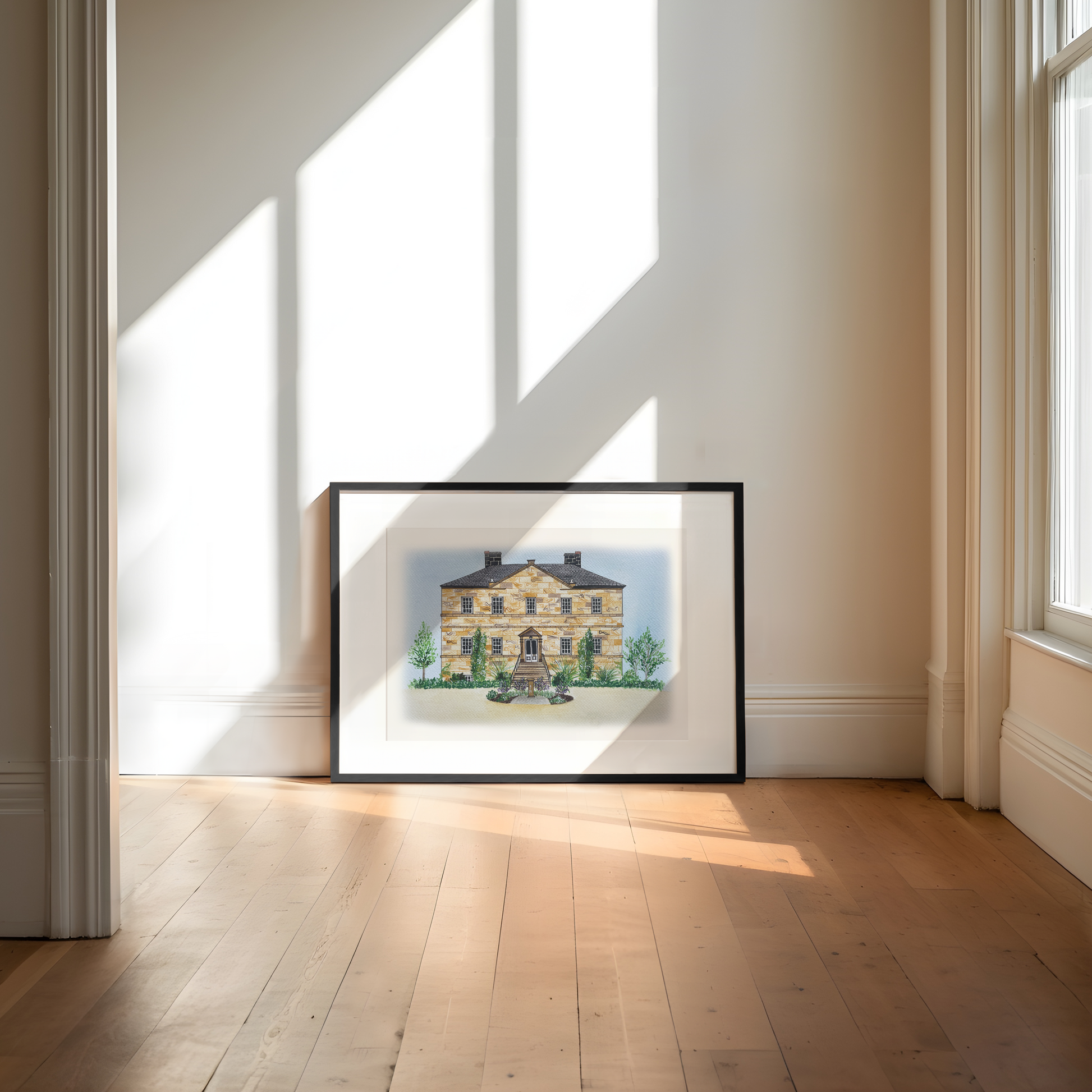 Framed artwork of a wedding venue on a white background in a bright room with large windows.