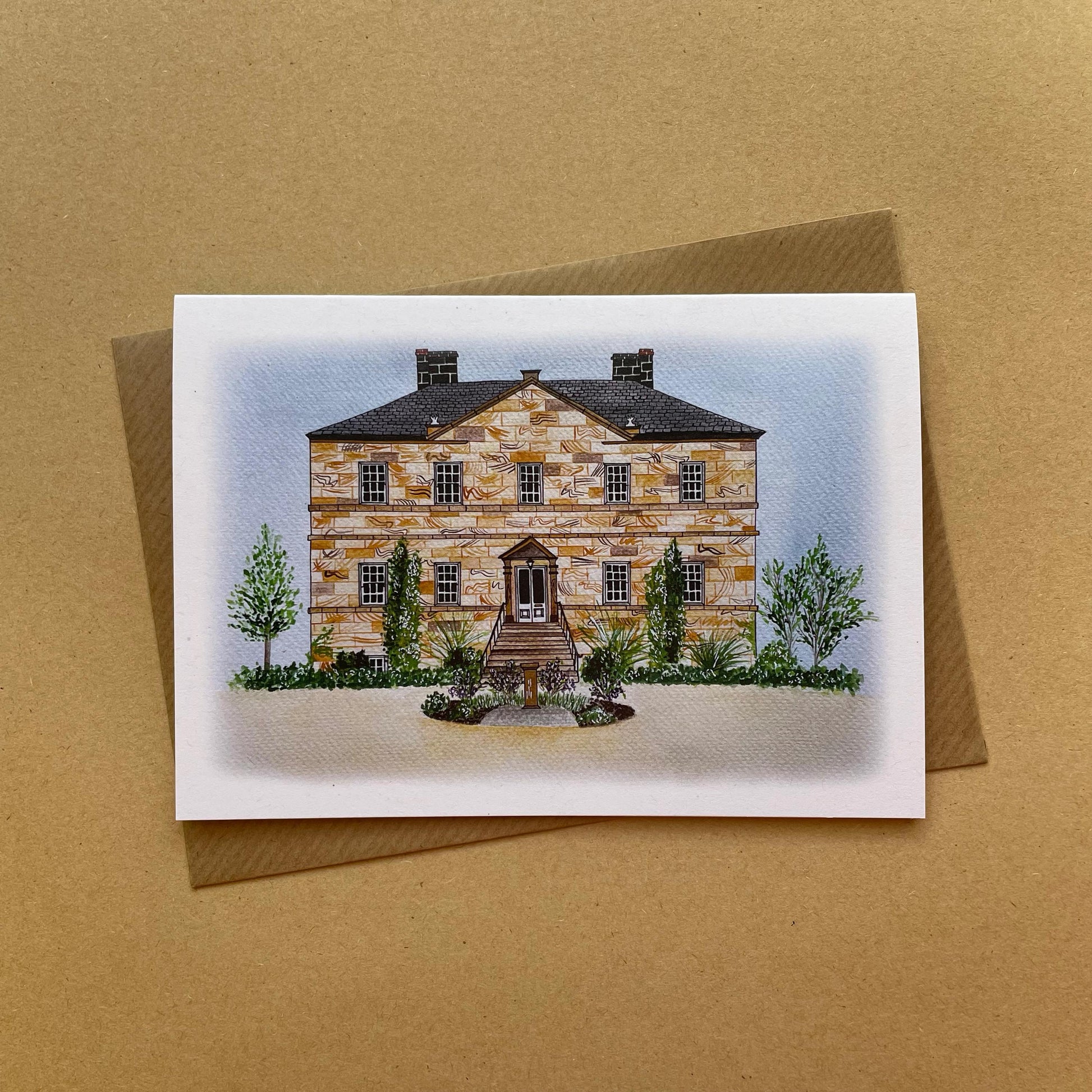 Greeting card with an illustration of Newton Hall wedding venue illustration displayed on a brown background