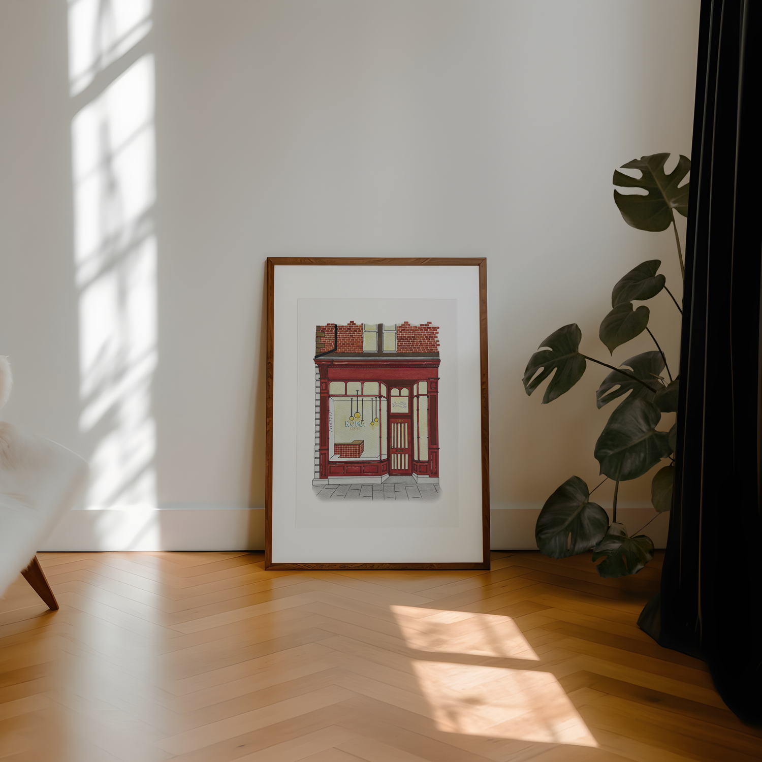 Framed artwork of Roma coffee shop on a wall with a plant and sunlight casting shadows on a wooden floor.