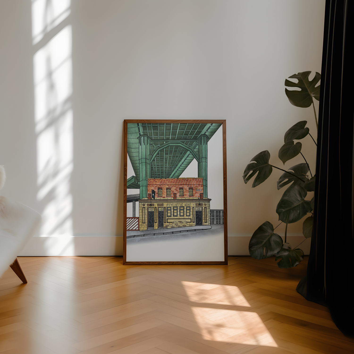 Framed artwork of the Bridge Tavern pub Newcastle on a wall with a plant and sunlight casting shadows on the floor