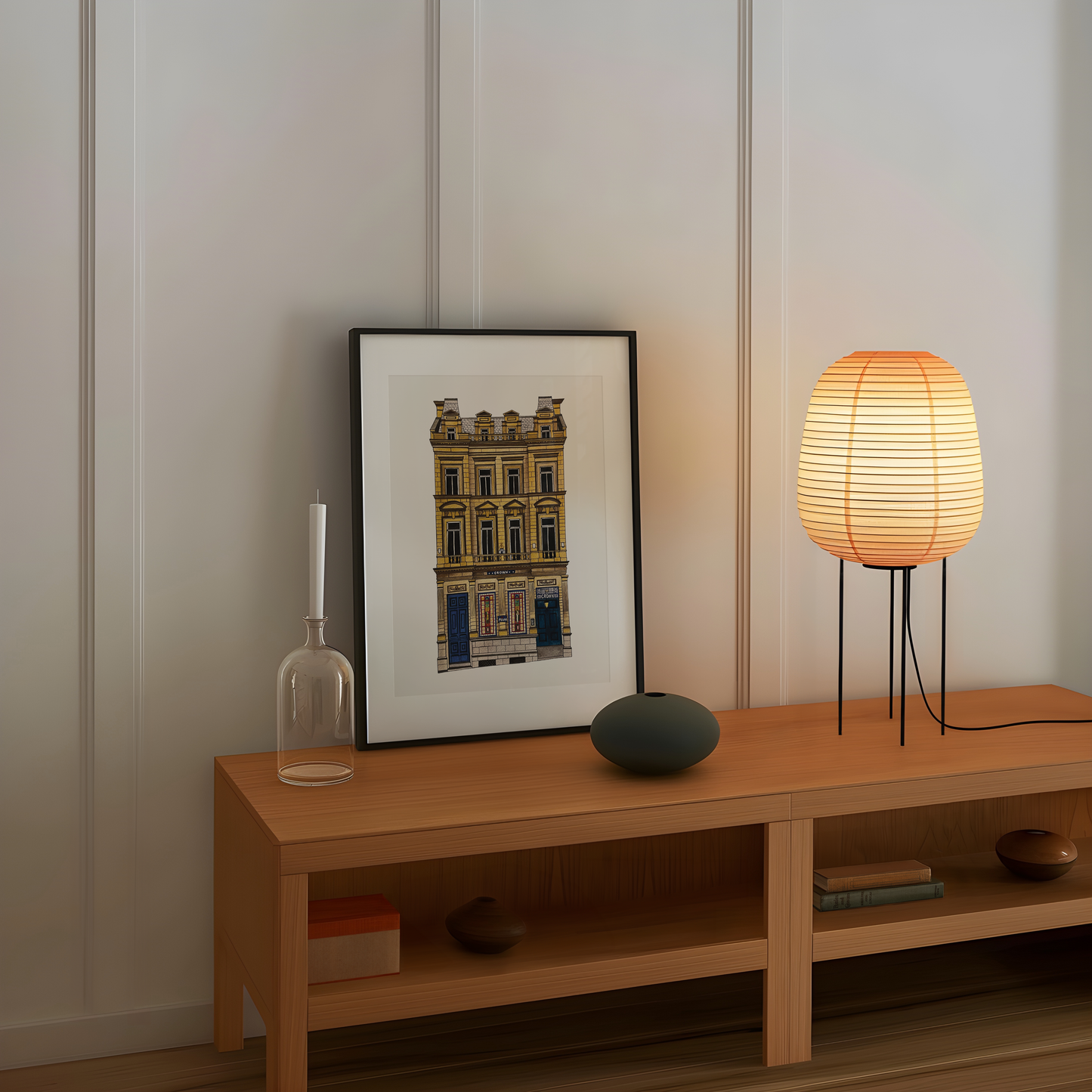 Wooden shelf with a framed picture of the crown posada, candle, vase, and lamp against a white wall.