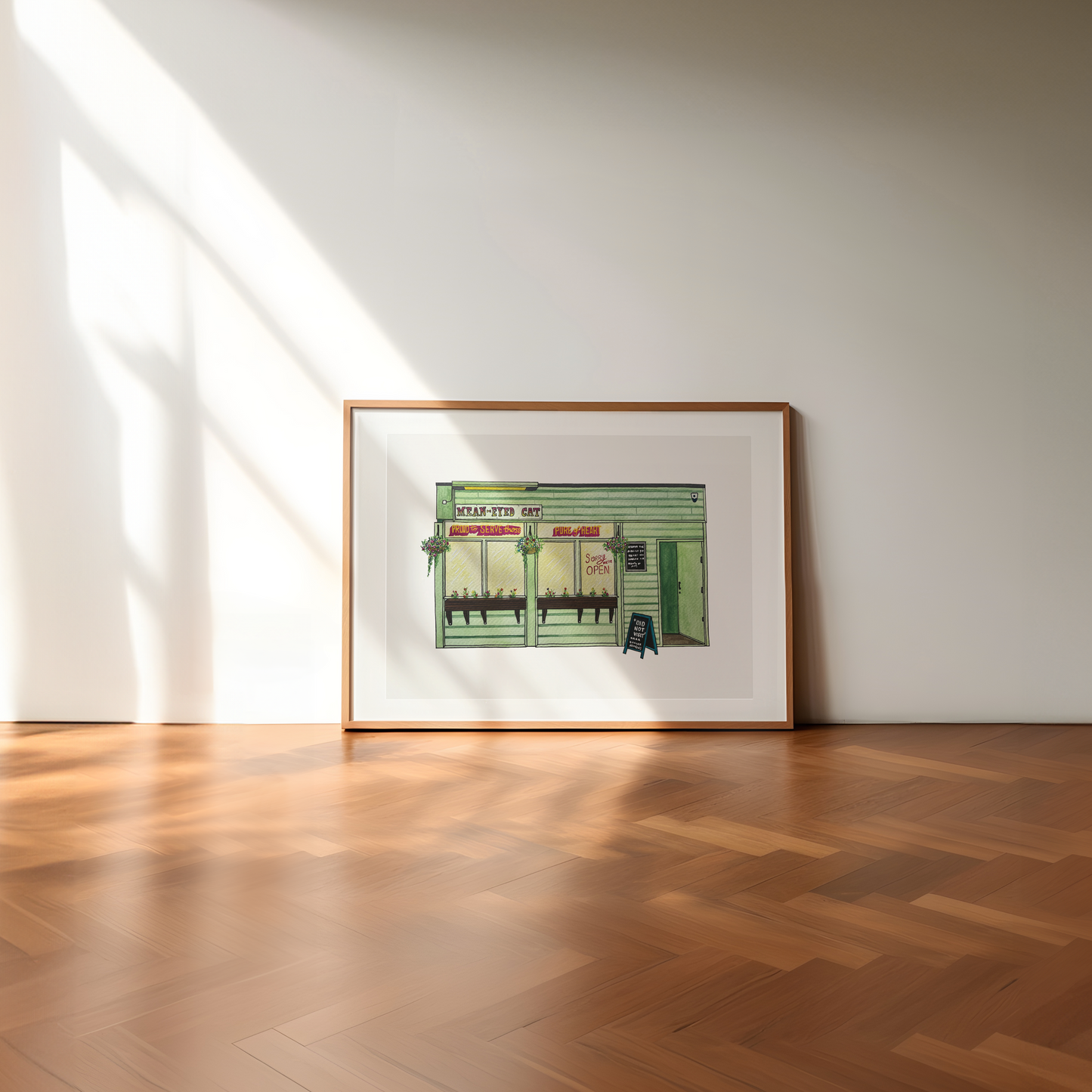 Framed artwork of The Mean Eyed Cat on a wall in a room with wooden flooring