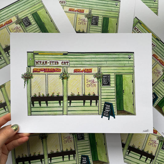 Illustration of the Mean Eyed Cat bar Newcastle held by a hand on a patterned background.