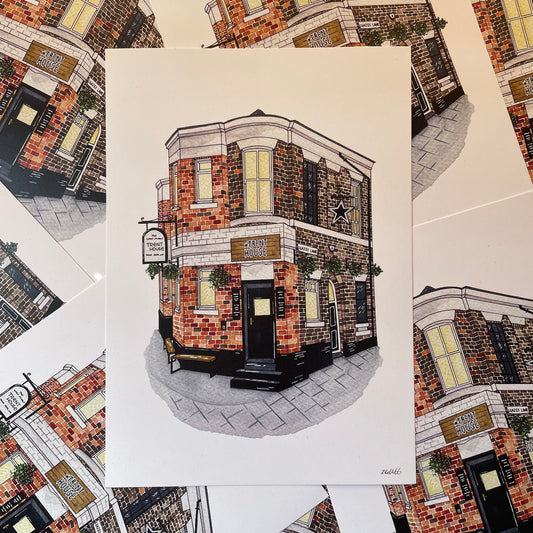 An art print featuring a detailed illustration of a brick pub building, displayed on top of several matching prints.