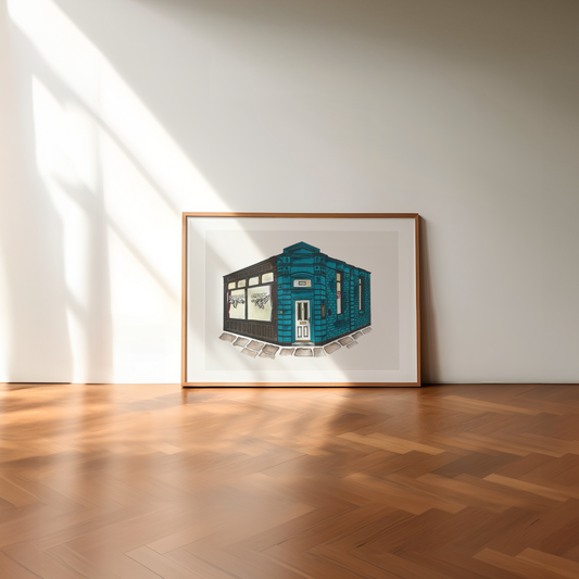 Framed artwork of a blue building on a white wall with wooden flooring
