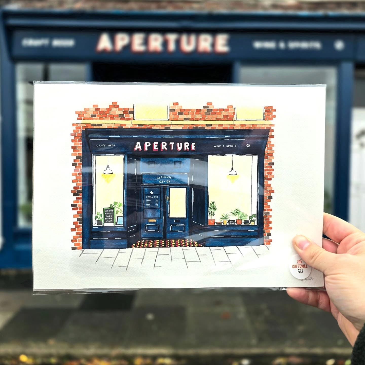 Illustration of a store front with 'APERTURE' branding held in front of a real store.