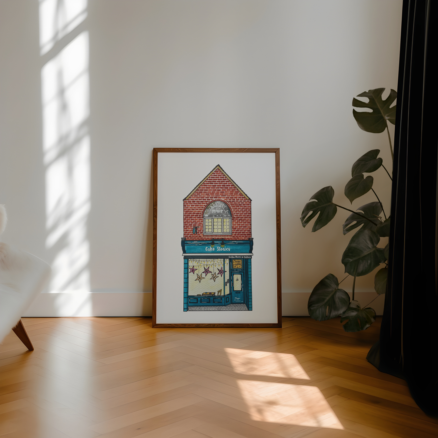 Framed artwork of cake stories jesmond building on a wall with sunlight casting shadows