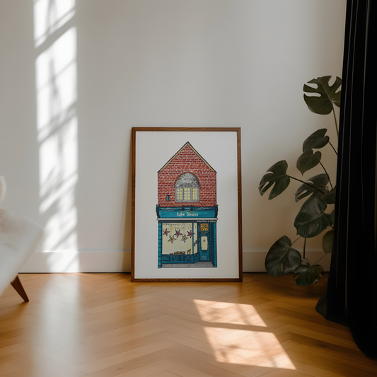 Framed artwork of cake stories jesmond building on a wall with sunlight casting shadows