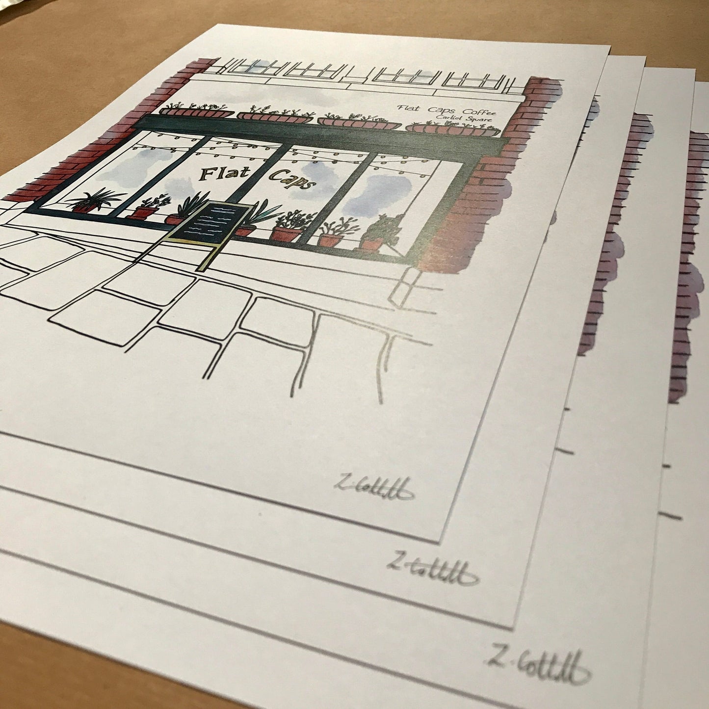 Printed design of a cafe window with 'Flat Caps' sign on a wooden surface