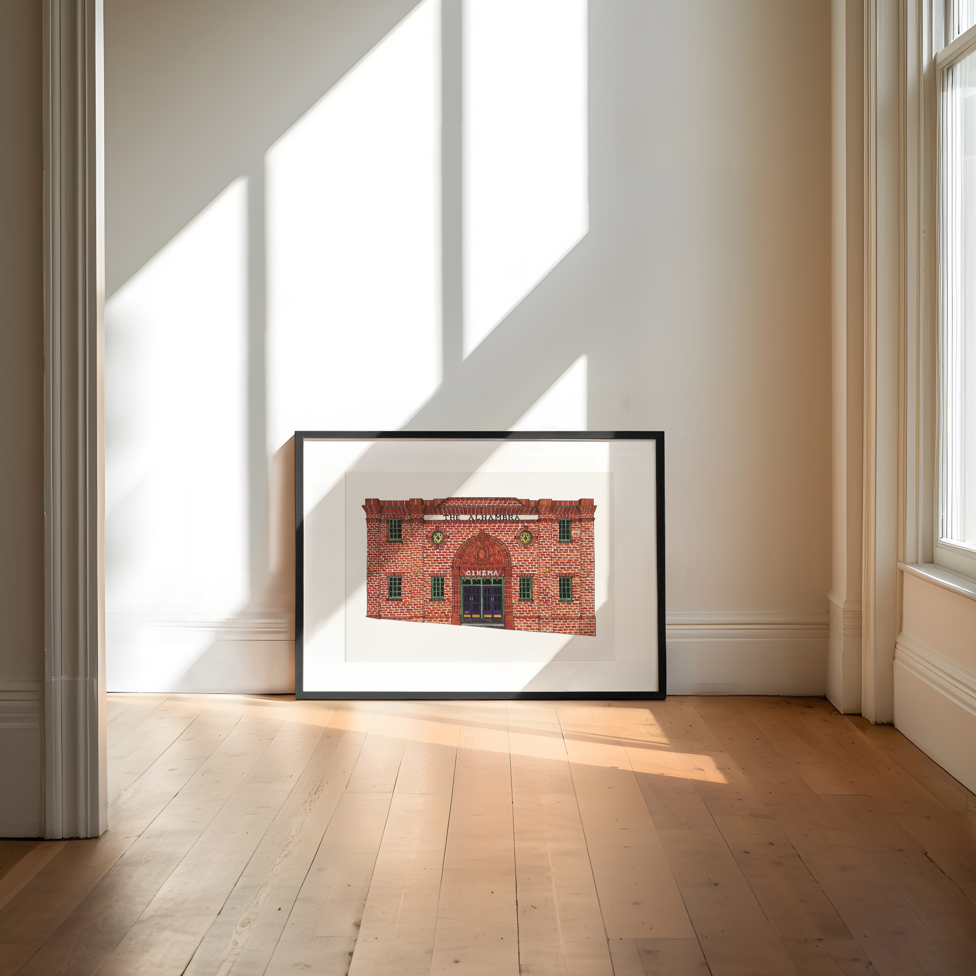 Framed print of a red brick building in a bright room with large windows.