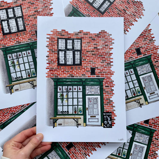 Hand holding a print of a brick building with green doors and windows.