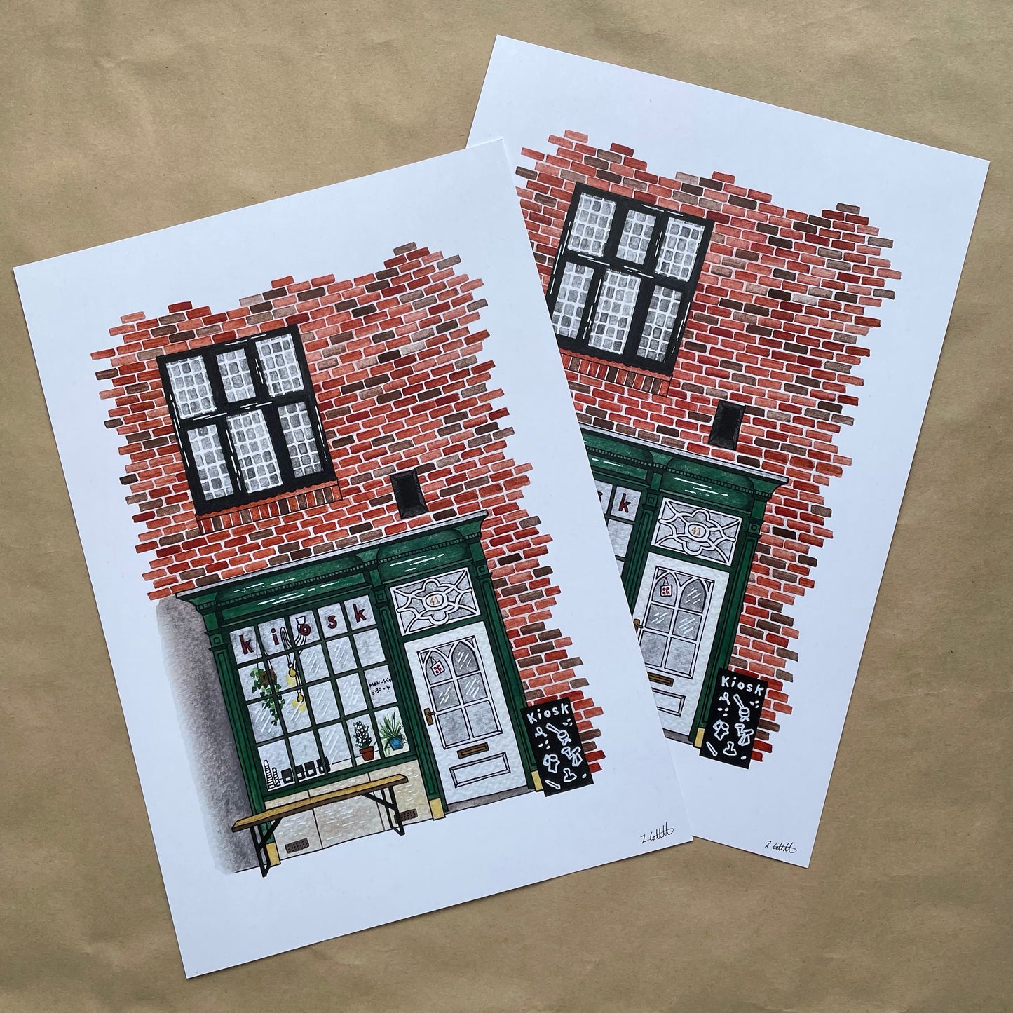Two illustrations of brick buildings with windows on white paper against a brown background.