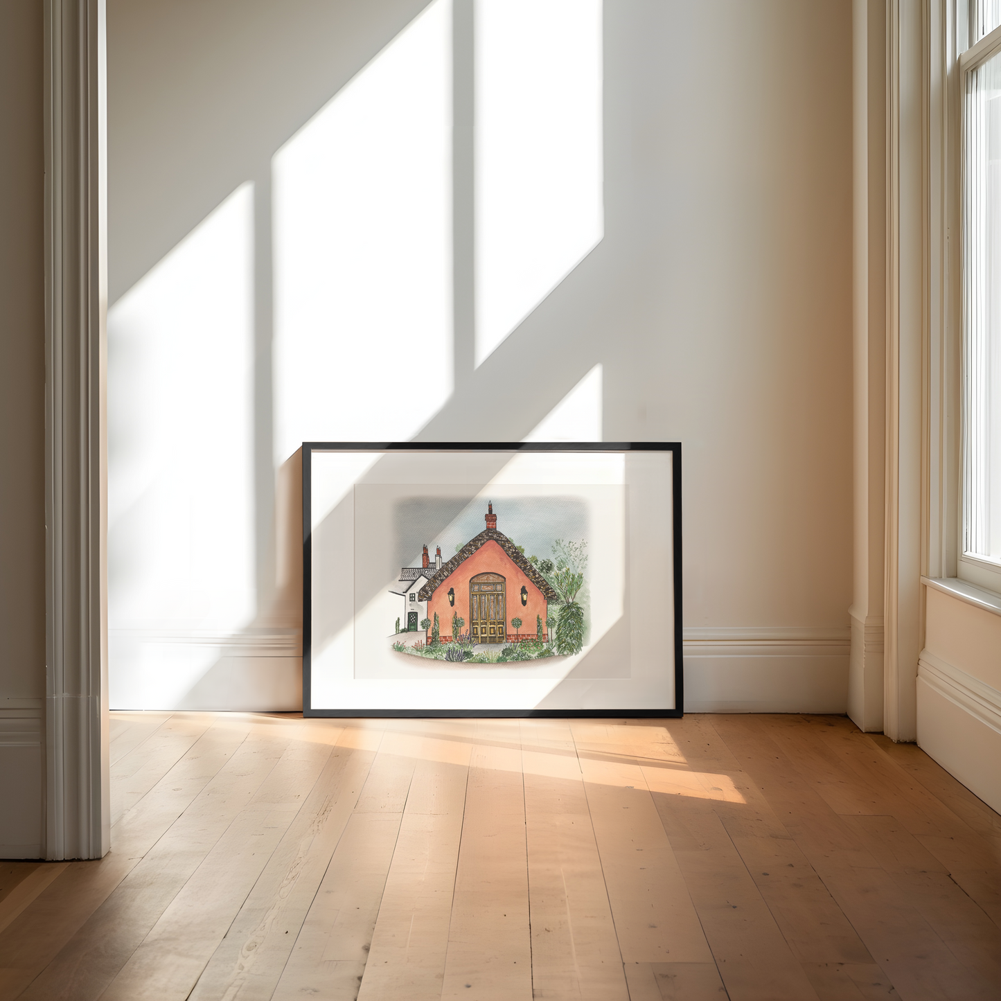 Framed artwork of le Petit Château wedding venue on a wall in a bright room with sunlight streaming through windows.