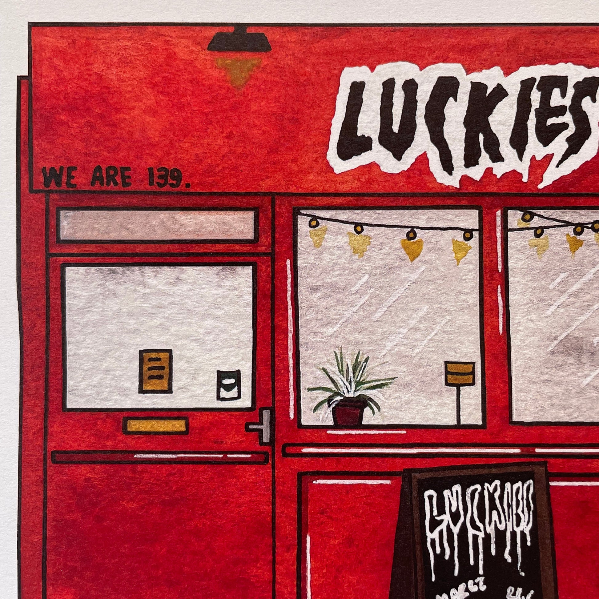 A close-up of a red illustrated storefront with the word 'LUCKIES' in large white letters, plus smaller text reading 'WE ARE 139.' and a chalkboard sign.