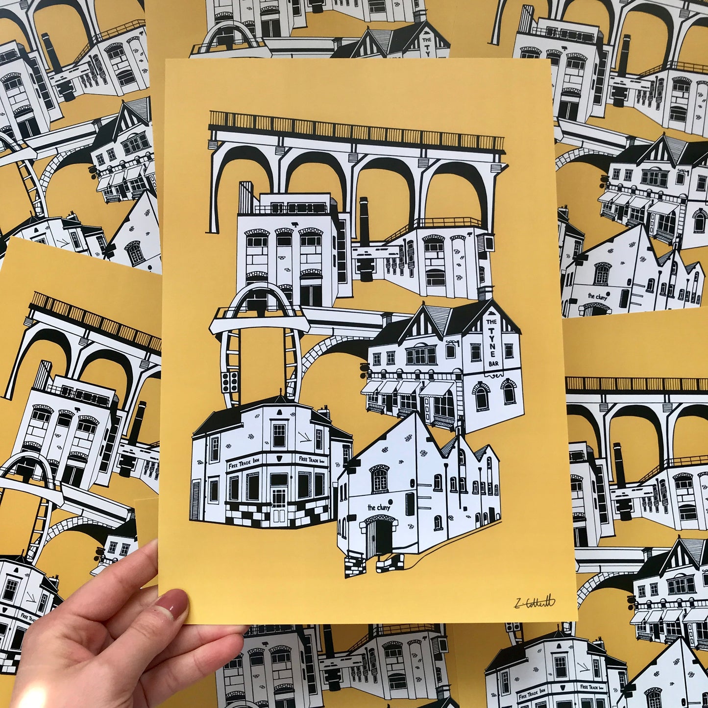 Hand holding a framed illustration of architectural designs on a yellow background with more illustrations in the background.